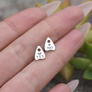 May include: Two silver charm pendants shaped like a witch's hat with the words "YES" and "NO" on them. The "YES" charm has a crescent moon and the "NO" charm has a star.