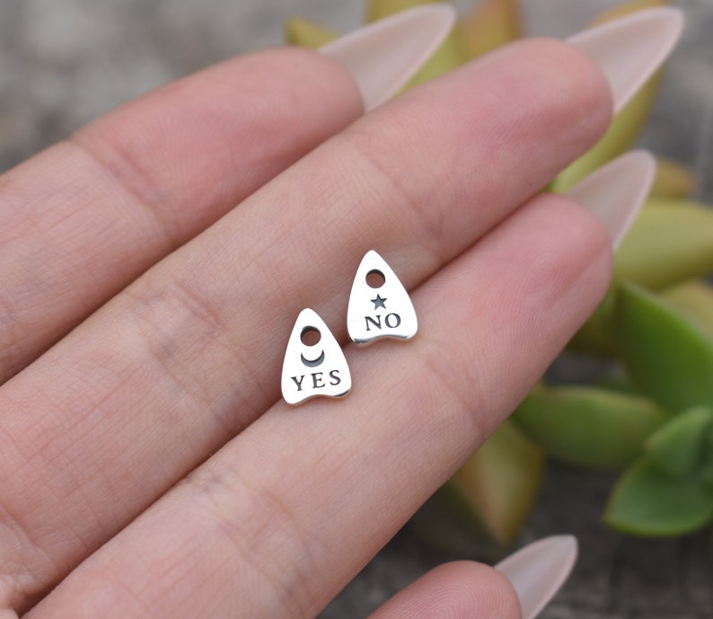 May include: Two silver charm pendants shaped like a witch's hat with the words "YES" and "NO" on them. The "YES" charm has a crescent moon and the "NO" charm has a star.