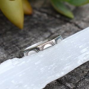 May include: A silver ring with a repeating pattern of sunbursts. The ring is thin and delicate.