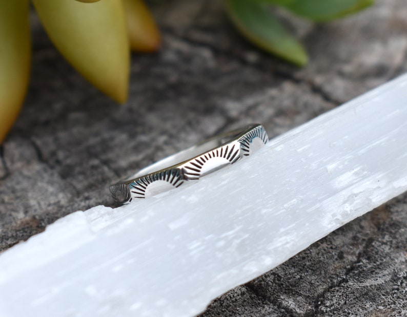 May include: A silver ring with a repeating pattern of sunbursts. The ring is thin and delicate.