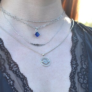 May include: A layered silver necklace with a blue gemstone pendant and a silver pendant with a sun and moon design.