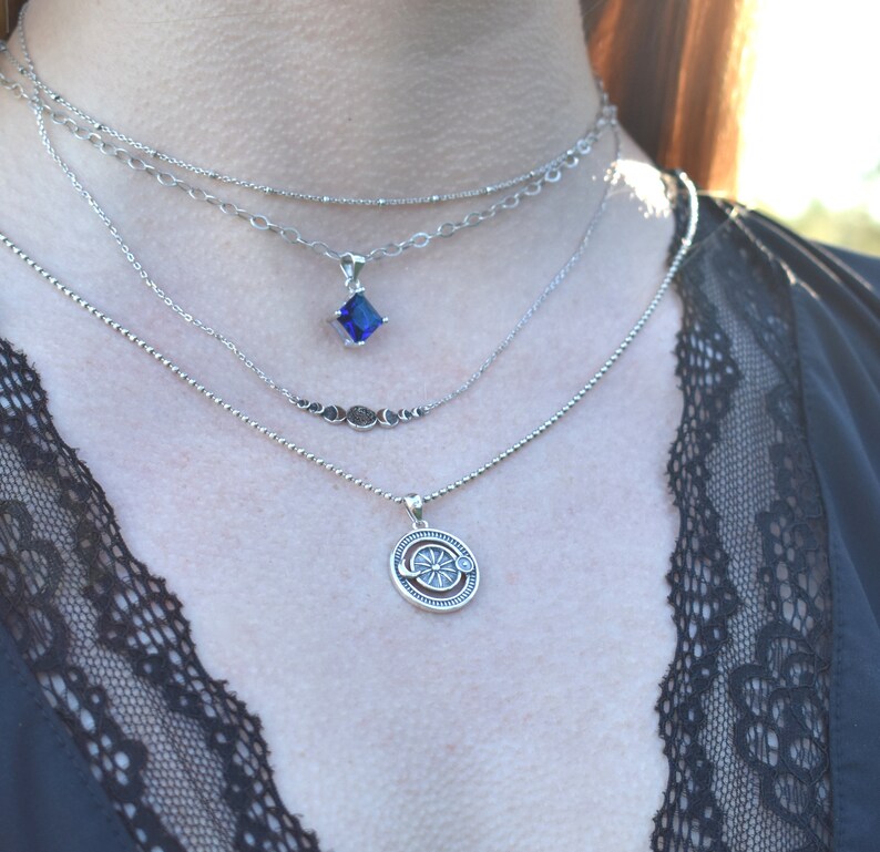 May include: A layered silver necklace with a blue gemstone pendant and a silver pendant with a sun and moon design.