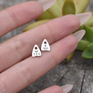 May include: Two silver charm pendants shaped like a witch's hat. One charm says "YES" with a crescent moon and sun symbol. The other charm says "NO" with a star symbol.