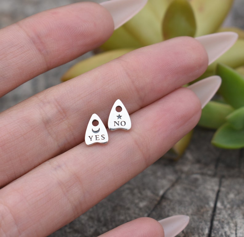 May include: Two silver charm pendants shaped like a witch's hat. One charm says "YES" with a crescent moon and sun symbol. The other charm says "NO" with a star symbol.
