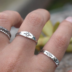 May include: Two silver rings with celestial designs. One ring features a star, the other features a crescent moon, a star, and a sun.