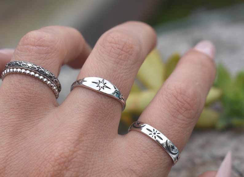 May include: Two silver rings with celestial designs. One ring features a star, the other features a crescent moon, a star, and a sun.