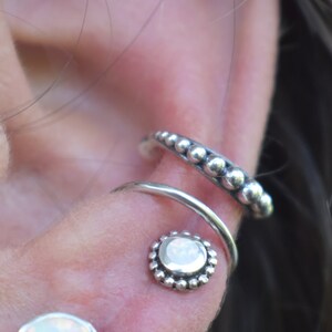 May include: A close-up of a silver ear cuff with a row of small beads and a silver hoop with a white opal stone in the centre.