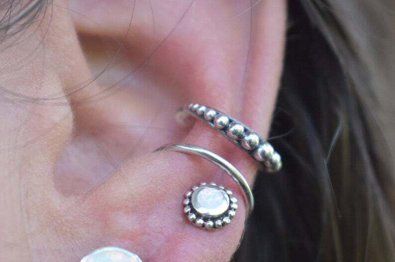 May include: A close-up of a silver ear cuff with a row of small beads and a silver hoop with a white opal stone in the centre.