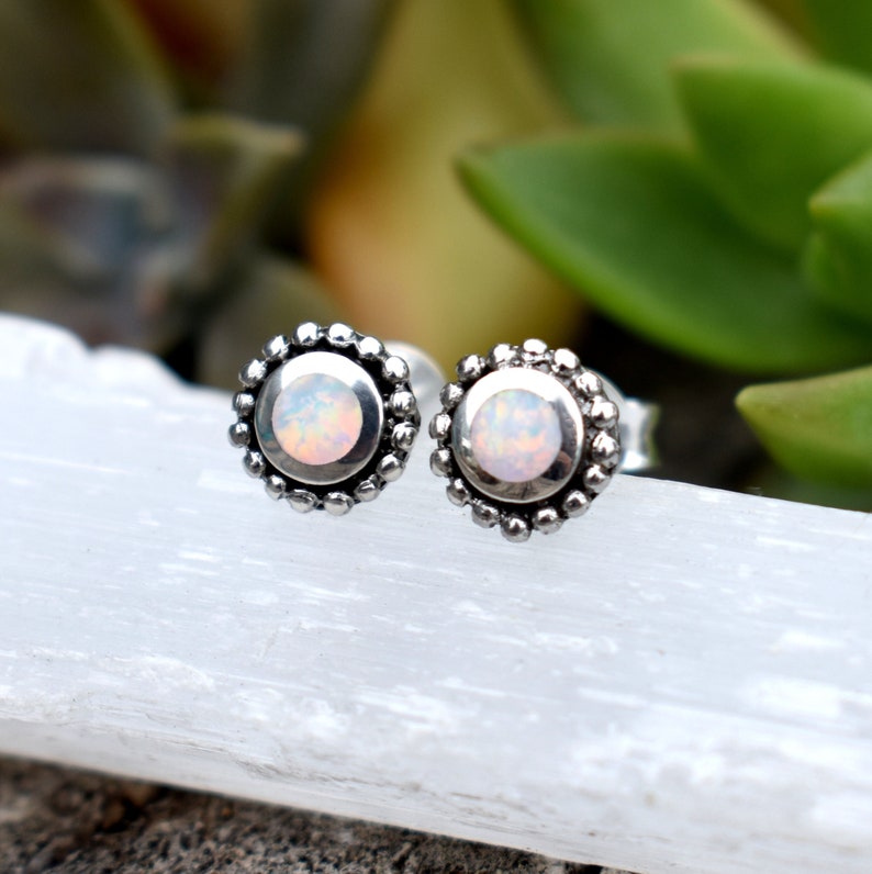 May include: A pair of silver stud earrings with a small, round, iridescent opal stone set in each earring. The earrings have a beaded border around the stone.