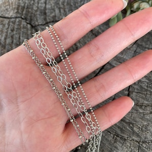 May include: Four silver chains of different styles and lengths, including a delicate chain with small beads, a thicker chain with larger beads, and two chain link styles.