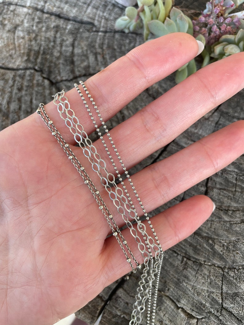 May include: Four silver chains of different styles and lengths, including a delicate chain with small beads, a thicker chain with larger beads, and two chain link styles.