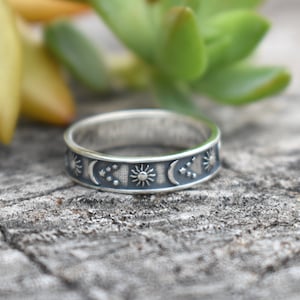 May include: A silver band ring with a celestial design featuring suns, moons, and stars.