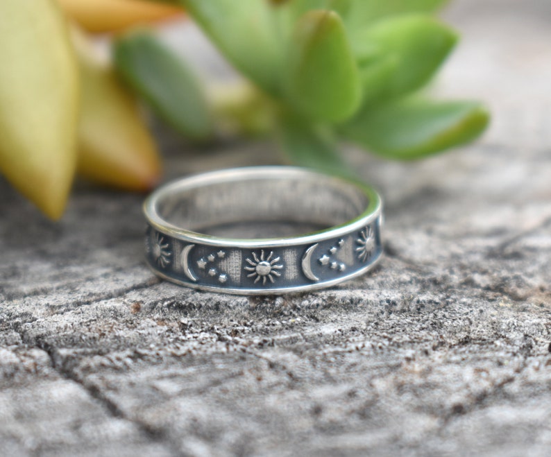 May include: A silver band ring with a celestial design featuring suns, moons, and stars.