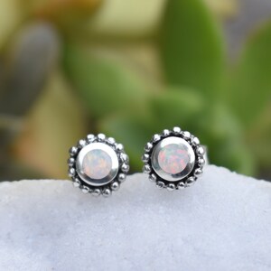 May include: A pair of silver stud earrings with a white opal gemstone in the centre of each earring. The earrings have a beaded border.