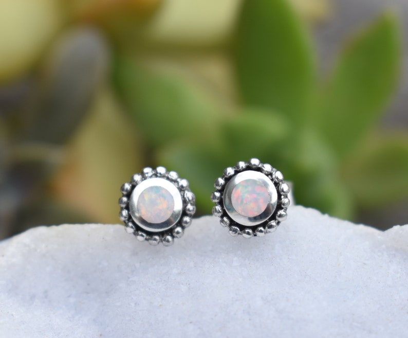 May include: A pair of silver stud earrings with a white opal gemstone in the centre of each earring. The earrings have a beaded border.