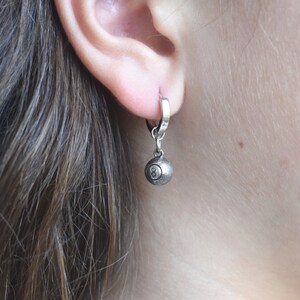 May include: Silver hoop earrings with a silver 8-ball charm hanging from the bottom.