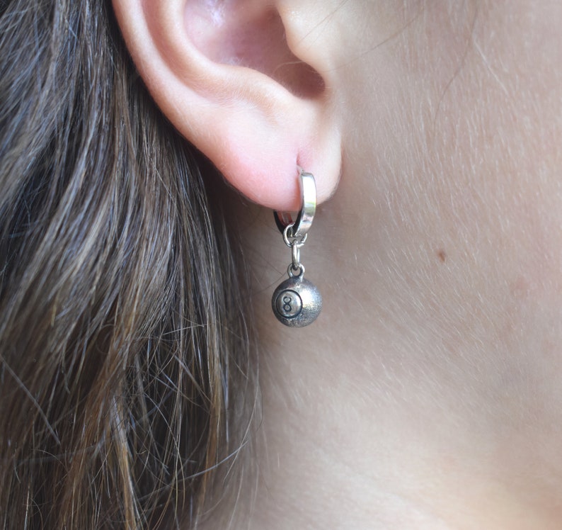May include: Silver hoop earrings with a silver 8-ball charm hanging from the bottom.