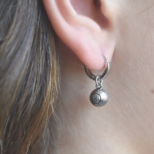 May include: Silver hoop earrings with a silver 8-ball charm hanging from the bottom.