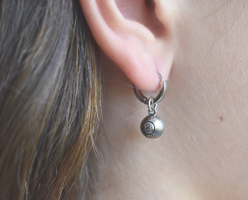 May include: Silver hoop earrings with a silver 8-ball charm hanging from the bottom.