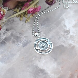 May include: A silver necklace with a circular pendant featuring a sun and moon design. The pendant has a textured, detailed design and is on a silver ball chain.
