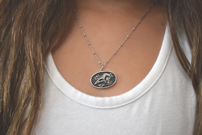 May include: A silver chain necklace with a pendant featuring a detailed skull design with floral accents.