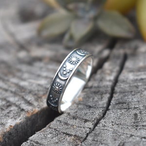 May include: A silver ring with a black oxidized finish. The ring features a design of a crescent moon, stars, and a sun.