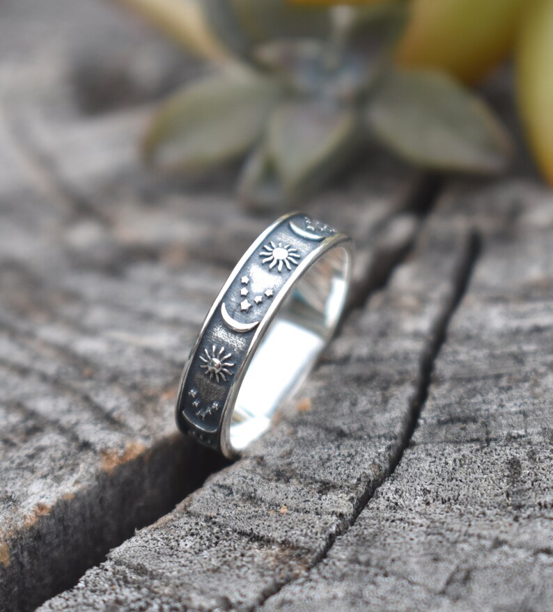 May include: A silver ring with a black oxidized finish. The ring features a design of a crescent moon, stars, and a sun.