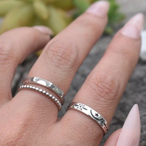 May include: Three silver rings with different designs. The first ring has a beaded band with a sun design. The second ring has a sun design. The third ring has a moon and star design.