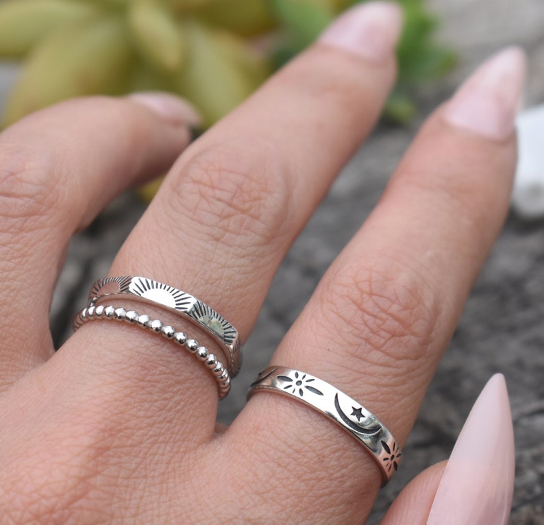 May include: Three silver rings with different designs. The first ring has a beaded band with a sun design. The second ring has a sun design. The third ring has a moon and star design.