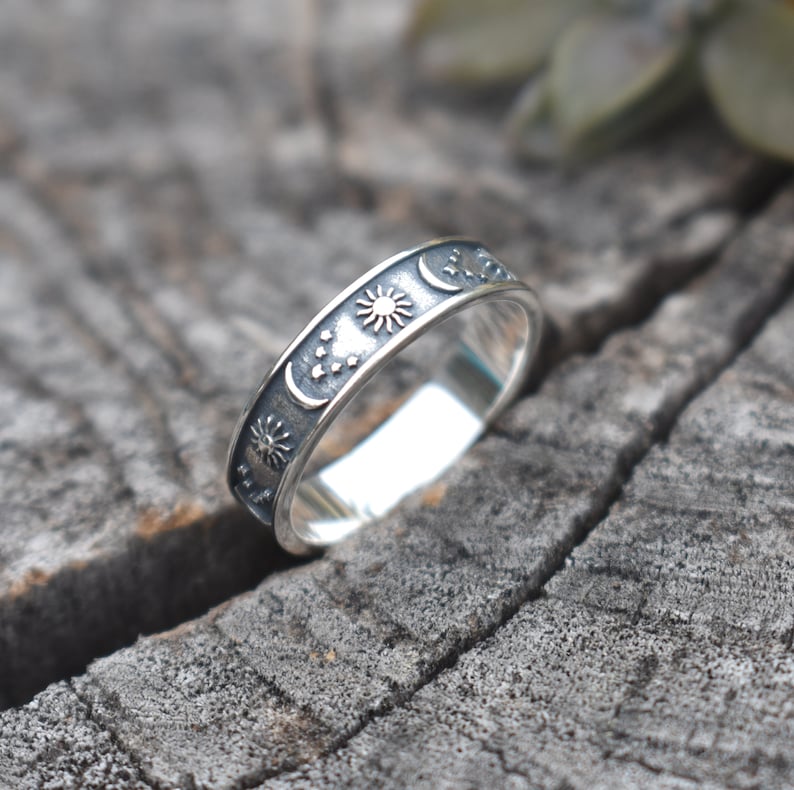 May include: A silver ring with a sun, moon, and stars design. The ring is on a wooden surface.
