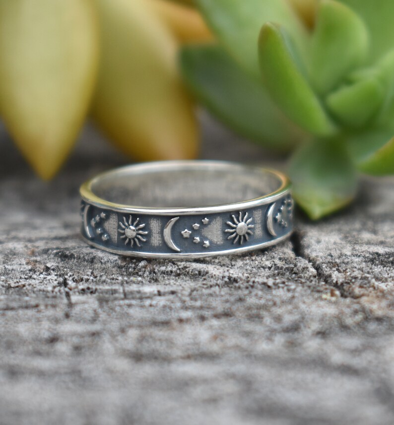 May include: A silver ring with a celestial design featuring moons, stars, and suns. The ring is on a wooden surface.