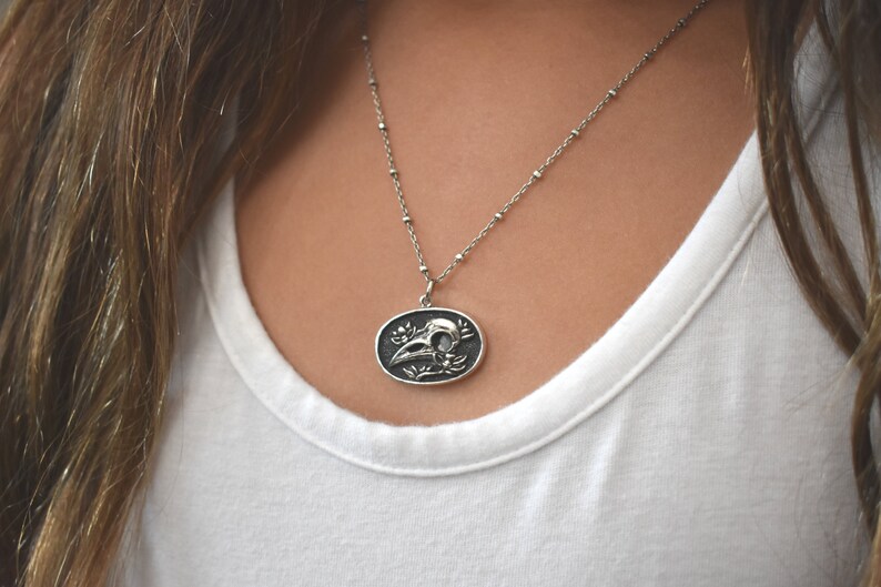 May include: A silver chain necklace with a pendant featuring a detailed skull with floral accents.