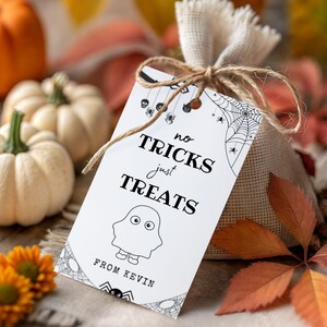 May include: A burlap gift bag tied with twine, featuring a white tag with the text "no tricks just treats" and a ghost illustration. The tag also includes the text "from Kevin". Pumpkins and fall foliage are in the background.