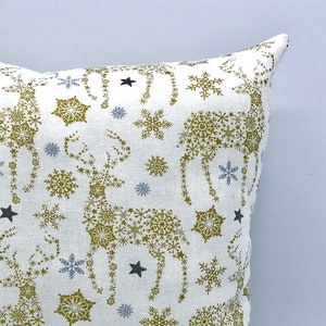 May include: White throw pillow with a gold and blue snowflake pattern featuring reindeer made of snowflakes.