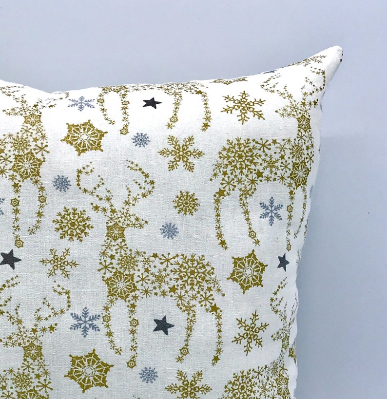 May include: White throw pillow with a gold and blue snowflake pattern featuring reindeer made of snowflakes.