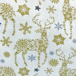 May include: White fabric with a repeating pattern of gold snowflakes and stars forming the shape of a reindeer.