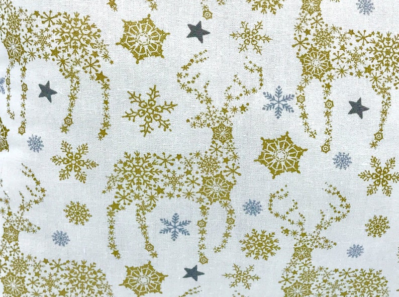 May include: White fabric with a repeating pattern of gold snowflakes and stars forming the shape of a reindeer.