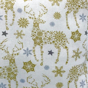 May include: White fabric with a repeating pattern of gold snowflakes and stars. The snowflakes are arranged to form the shape of a reindeer.