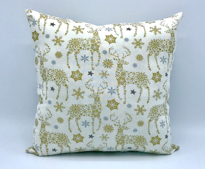 May include: White throw pillow with a gold and blue snowflake pattern and reindeer silhouettes.