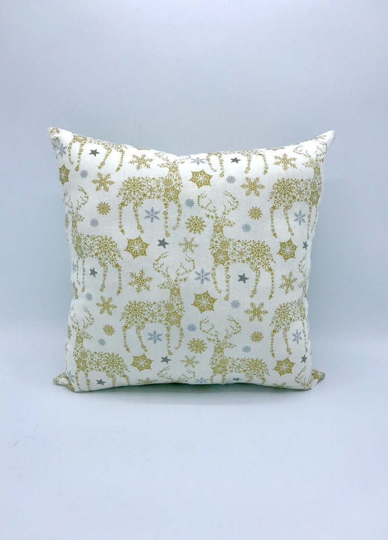 May include: A white throw pillow with a gold and silver snowflake and reindeer pattern.