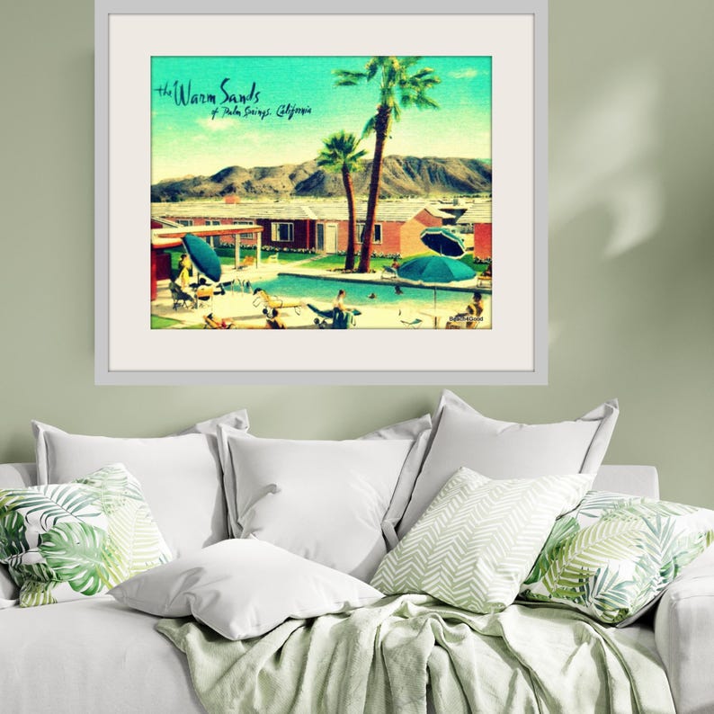 May include: Framed vintage-style print titled "The Warm Sands of Palm Springs, California." The artwork depicts a retro scene with a swimming pool, palm trees, and mid-century modern buildings, evoking a sense of leisure and vacation.