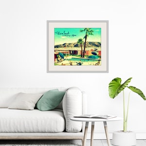 May include: Framed art print featuring a vintage-style illustration of a mid-century modern resort scene. The artwork depicts a swimming pool, palm trees, and a retro building, with the text "the Warm Sands, Palm Springs, California". The print is displayed on a white wall.
