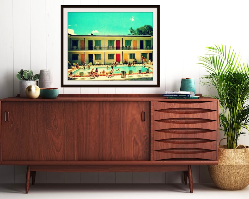 Pode incluir: Uma fotografia emoldurada de um motel vintage com uma piscina. O motel tem portas coloridas e uma piscina turquesa. As pessoas est&atilde;o nadando e relaxando na piscina.