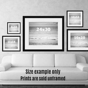 May include: A collection of framed prints in various sizes, including 8x10, 11x14, 12x12, 16x20, and 24x30 inches, displayed on a wall. The prints feature a black and white seascape. The text "Size example only Prints are sold unframed" is visible.