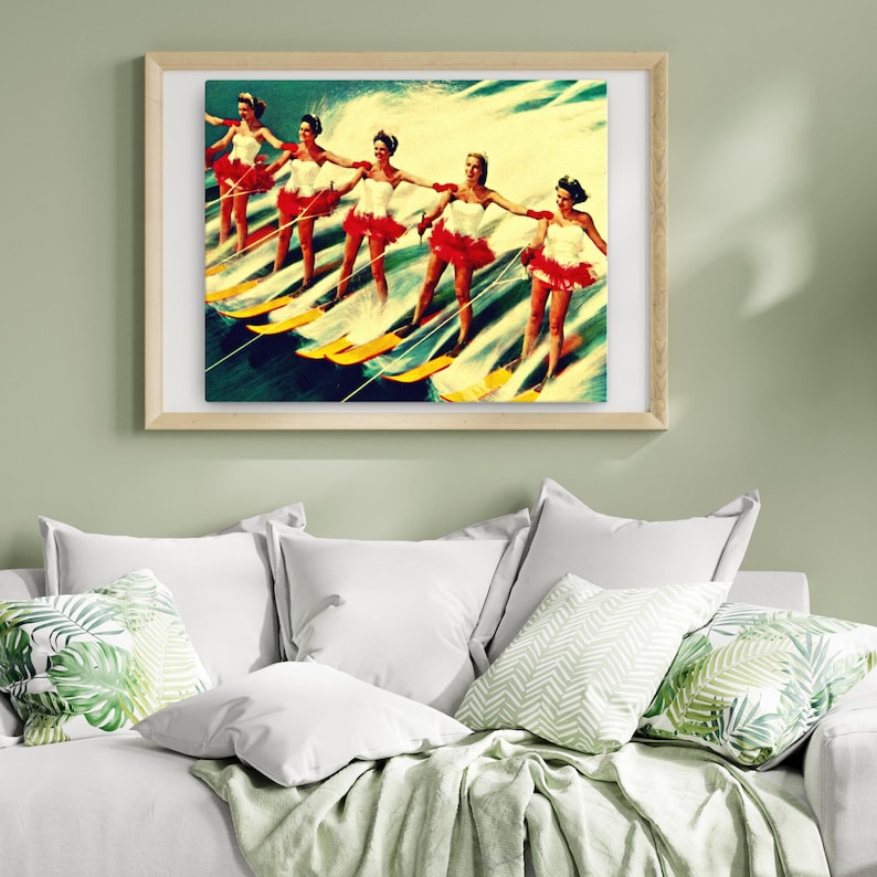 May include: A vintage illustration of six women water skiing in a line, wearing red and white dresses. The women are smiling and holding onto their skis. The water is blue and green, and the sky is a light blue. The image is in a wooden frame.