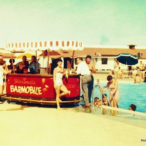 Pode incluir: Um barm&oacute;vel vermelho e branco com o texto "Hacienda Barm&oacute;vel" no lado. O barm&oacute;vel est&aacute; localizado junto a uma piscina com pessoas nadando e relaxando ao redor.