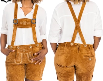Puede incluir: Un conjunto de cuero marrón de dos piezas, con pantalones cortos con tirantes. Los pantalones cortos tienen un bolsillo delantero y costuras decorativas. Los tirantes se sujetan con hebillas metálicas. El conjunto se lleva sobre una camisa blanca.