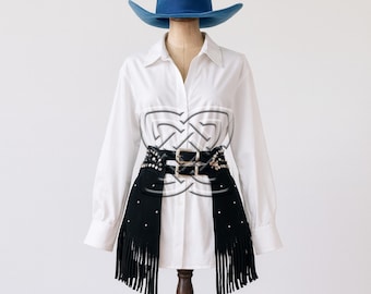 May include: A white button-down shirt with a black fringed belt and a blue hat. The belt has silver studs and a double buckle. The word "Snazzy" is in the upper left corner.