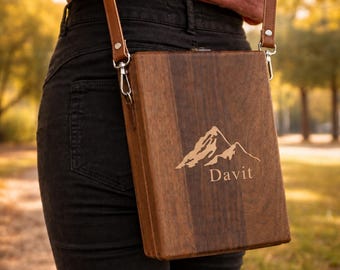 May include: A rectangular wooden crossbody bag with a dark brown grain, featuring a laser-engraved mountain graphic and the text "Davit" on the front. The bag is attached to a thin brown leather strap with silver-toned metal hardware.