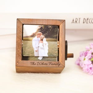 Op de afbeelding: Een houten fotolijst met een draaimechanisme, met een trouwfoto. De lijst is gegraveerd met "The White Family". De foto toont een stel dat buiten kust. De lijst heeft een warme bruine kleur.